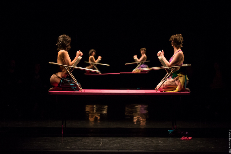 Molly and Eleanor sit atop a pink table. Their torsos are wedged between the opening in two chairs